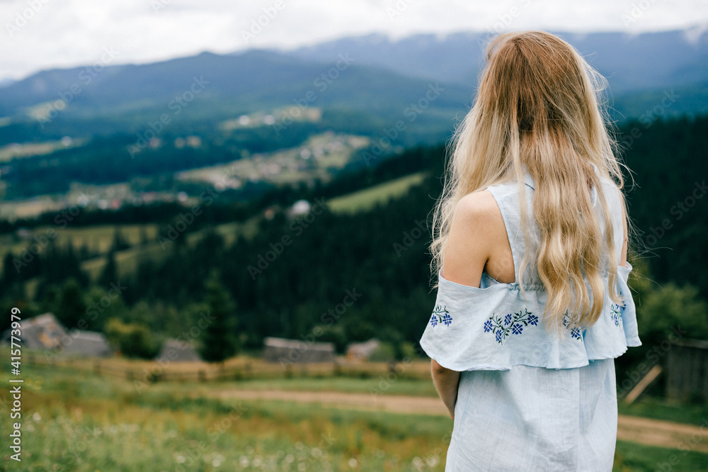 Young attractive elegant blonde girl in blue romantic dress posing back over picturesque landscape - obrazy, fototapety, plakaty 