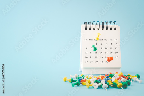 thumbtacks marked on white calendar page with blurred others on grunge blue paper background , due date ,appointment, payment, reminder or business concept