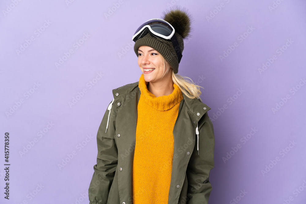 Skier Russian girl with snowboarding glasses isolated on purple background looking side Skier Russian girl with snowboarding glasses isolated on purple background looking side