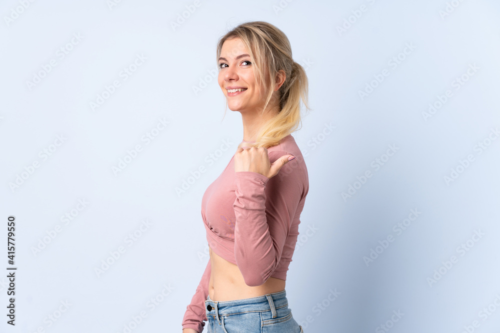 Blonde woman over isolated blue background pointing to the side to present a product Blonde woman over isolated blue background pointing to the side to present a product