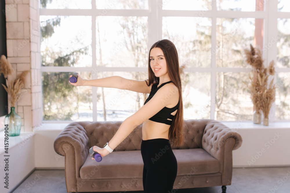 Attractive young woman training at home. Girl preparing for bikini season. Happy female use dumbbells for training Attractive young woman training at home. Girl preparing for bikini season. Happy female use dumbbells for training