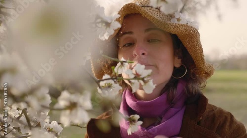 Woman smelling and touching branches of blooming almond trees in the field in Madrid at sunset. 