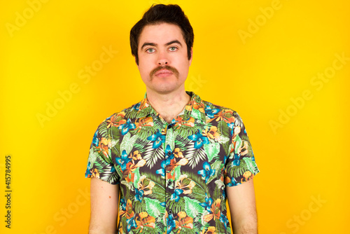 Wallpaper Mural Joyful young handsome Caucasian man wearing Hawaiian shirt against yellow wall looking to the camera, thinking about something. Both arms down, neutral facial expression. Torontodigital.ca