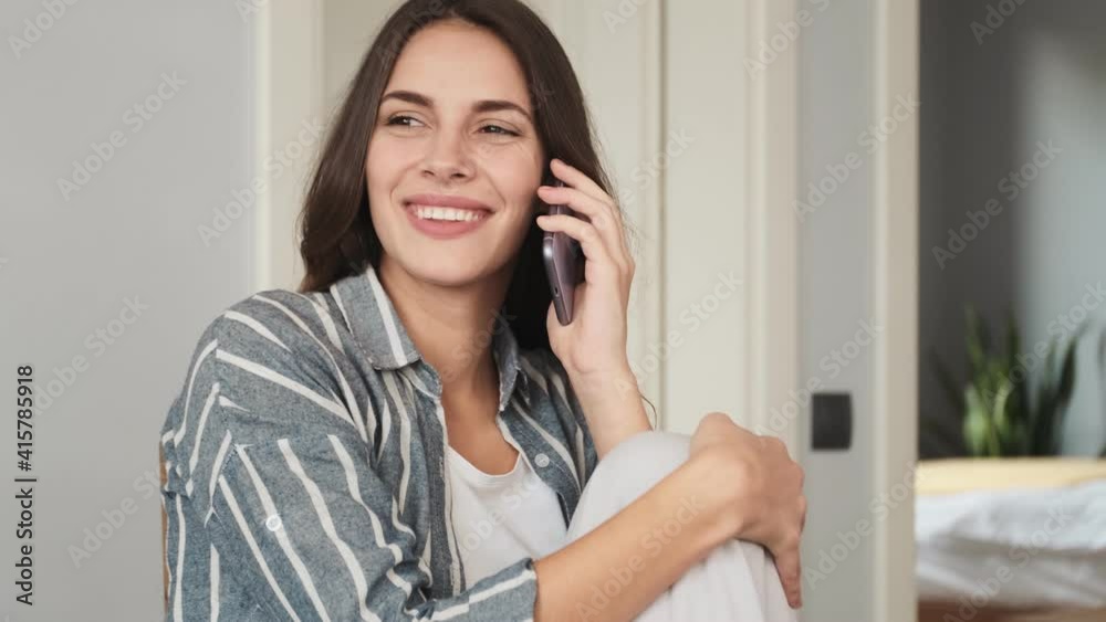 A beautiful young woman is talking on her smartphone sitting at home A beautiful young woman is talking on her smartphone sitting at home
