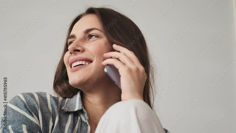 A close-up view of a smiling young woman is talking on her smartphone sitting at home A close-up view of a smiling young woman is talking on her smartphone sitting at home