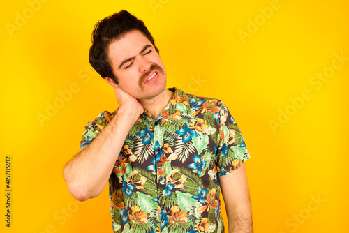 Wallpaper Mural young handsome Caucasian man wearing Hawaiian shirt against yellow wall suffering from back and neck ache injury, touching neck with hand, muscular pain. Torontodigital.ca