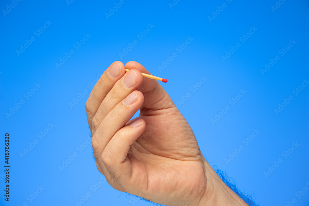 New unlit matchstick held in hand by Caucasian male hand studio shot isolated on blue New unlit matchstick held in hand by Caucasian male hand studio shot isolated on blue