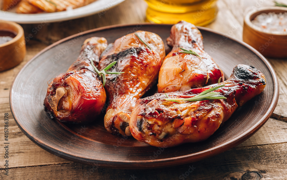 Chicken legs on brown plate with sauce and rosemary on wooden rustic background. Chicken legs on brown plate with sauce and rosemary on wooden rustic background.