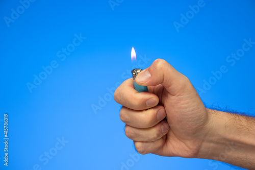 Caucasian male hand holding a lit manual lighter studio shot isolated on blue
