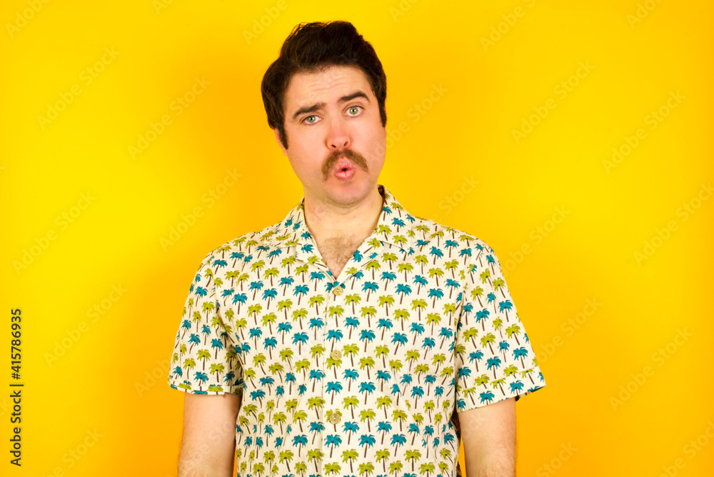young handsome Caucasian man wearing Hawaiian shirt against yellow wall expressing disgust, unwillingness, disregard having tensive look frowning face, looking indignant with something. young handsome Caucasian man wearing Hawaiian shirt against yellow wall expressing disgust, unwillingness, disregard having tensive look frowning face, looking indignant with something.
