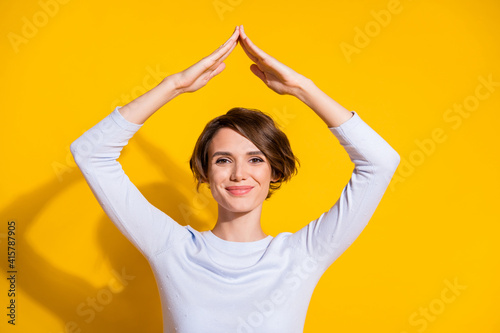 Photo of cheerful young lady hands roof look camera wear white shirt isolated yellow color background