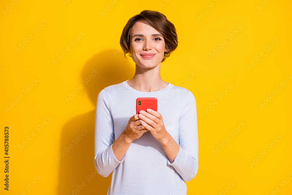 Photo portrait of happy woman holding phone in two hands isolated on bright yellow colored background Photo portrait of happy woman holding phone in two hands isolated on bright yellow colored background