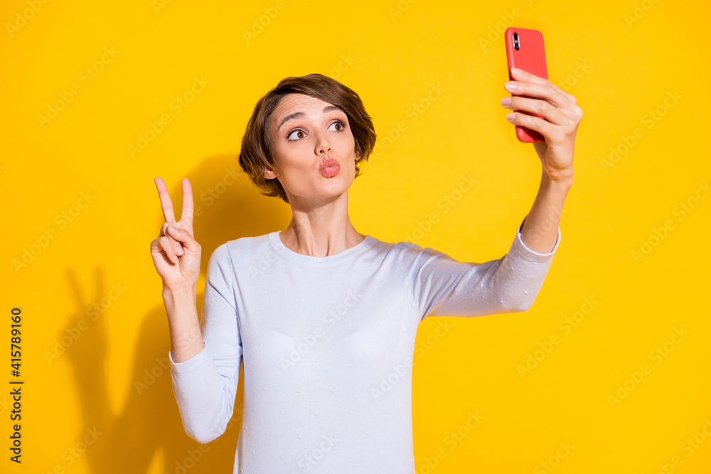 Photo of sweet pretty lady dressed white shirt tacking selfie modern gadget showing v-sign isolated yellow color background Photo of sweet pretty lady dressed white shirt tacking selfie modern gadget showing v-sign isolated yellow color background