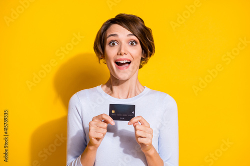 Photo of pretty charming young lady dressed white shirt holding bank credit card isolated yellow color background