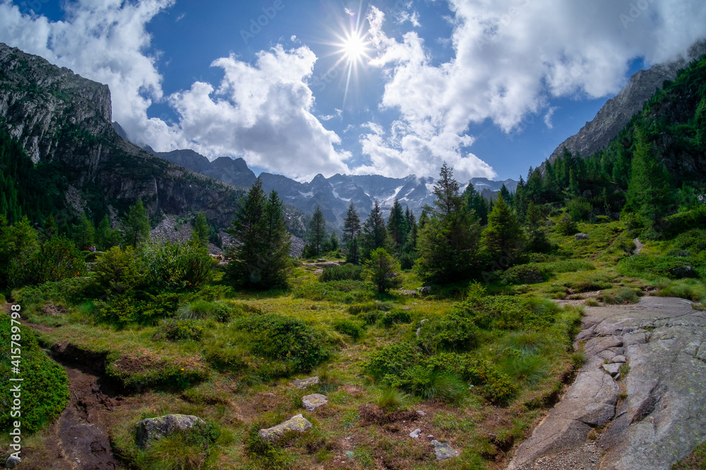 Panoramic view of mountain landscape in Italian Alps. Backlight photo of nature in green valley between sharp rocky mountain ridges.