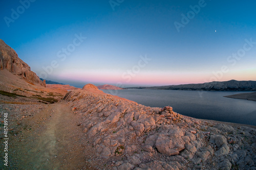 Morning panoramic view on rocky and arid landscape of Pag island on Adriatic coast in Croatia. Stones highlighted by colourful twilight light.