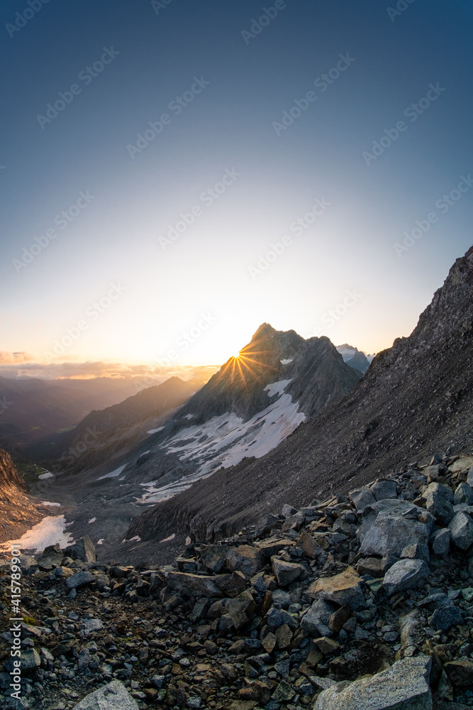 Sun rising behind mountain at Presena Glacier in Italian Alps. Picturesque view to deep valley lit by first sun rays of new day.