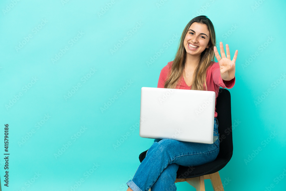 Young caucasian woman sitting on a chair with her pc isolated on blue background happy and counting four with fingers Young caucasian woman sitting on a chair with her pc isolated on blue background happy and counting four with fingers