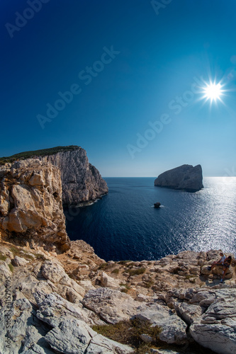 Picturesque view on coastal rock formation washed by calm sea at Capo Caccia. View against sun. Summer sunny day view clear sky.