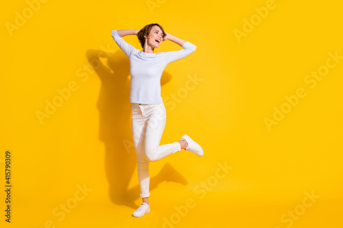 Photo of funny young lady hands head dance look empty space wear white shirt isolated yellow color background