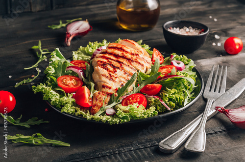 Grilled chicken fillet and fresh vegetable salad of tomatoes and arugula leaves. Healthy food. Black background.