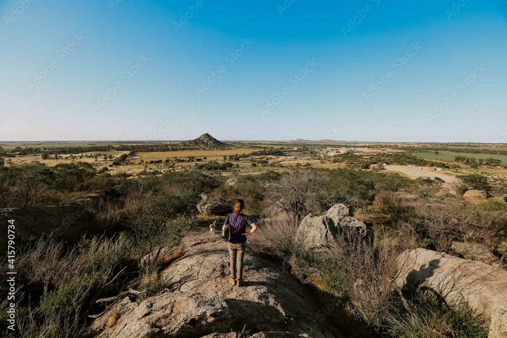 Woman exploring dry rocky outcrop in Central Victoria, Australia with view of Pyramid Hill in distance