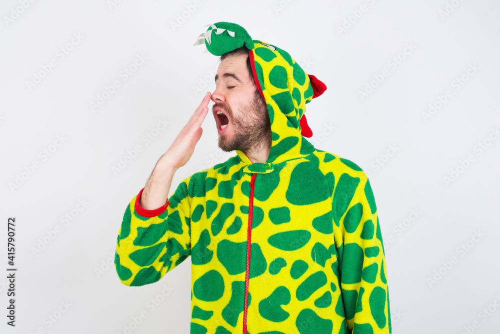 Fototapeta premium young caucasian man wearing a pajama standing against white wall being tired and yawning after spending all day at work.