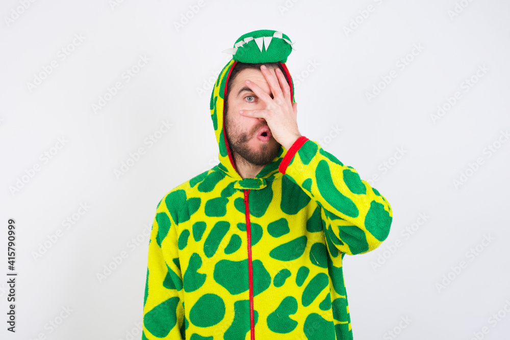 young caucasian man wearing a pajama standing against white background peeking in shock covering face and eyes with hand, looking through fingers with embarrassed expression. young caucasian man wearing a pajama standing against white background peeking in shock covering face and eyes with hand, looking through fingers with embarrassed expression.