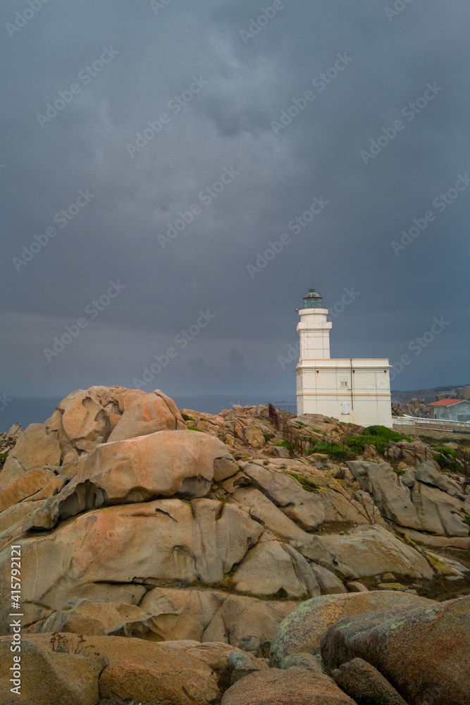 Lighthouse of Capo Testa, Sardinia, Italy. White building behind erosion rounded rocks. Overcast sky before storm.