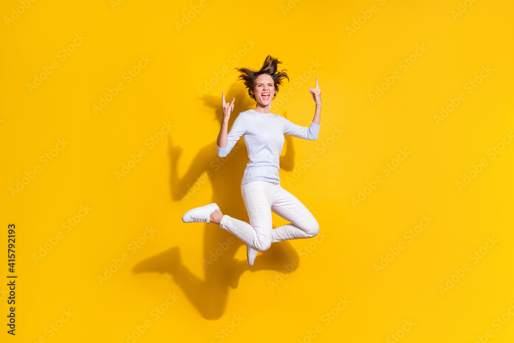 Photo of lady jump open mouth raise horns signs wear white shirt trousers sneakers isolated yellow color background