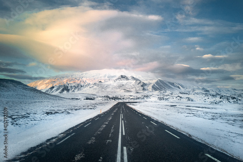 Empty asphalt road leading to snowy mountain range. Nordic winter landscape in Iceland. Clear road for safety transport.