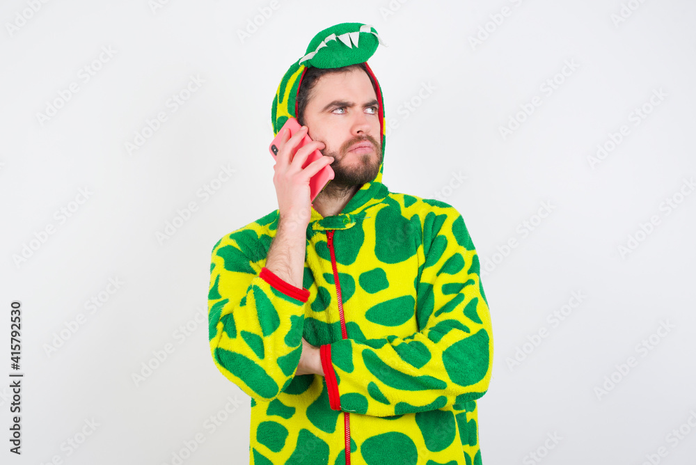 Sad young caucasian man wearing a pajama standing against white background talking on smartphone. Communication concept. Sad young caucasian man wearing a pajama standing against white background talking on smartphone. Communication concept.