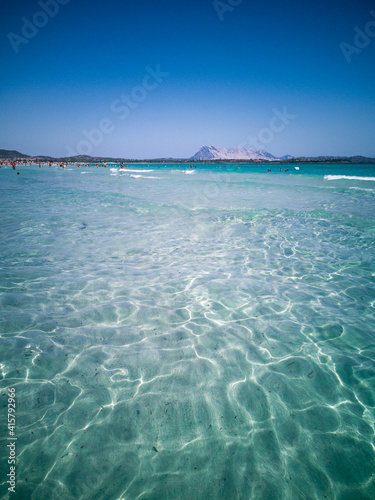 Sun light reflections in shallow water on sandy beach. Crowded beach in background. Summer vacation concept.