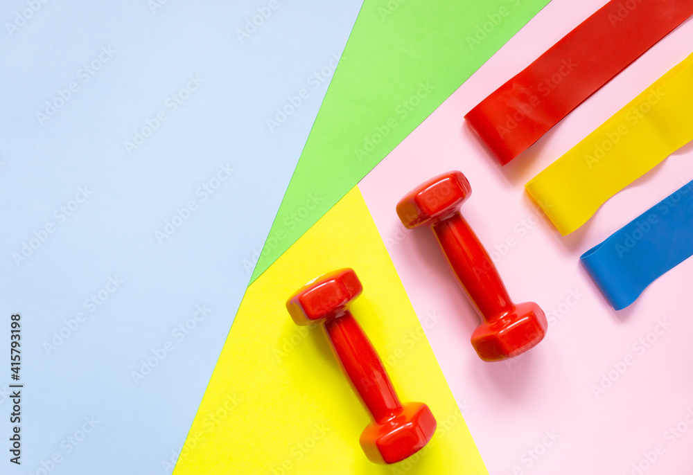 Red weights and rubber bands for sports on a colorful background. The concept of movement, sports, and a healthy lifestyle. Top view, free space for text. Red weights and rubber bands for sports on a colorful background. The concept of movement, sports, and a healthy lifestyle. Top view, free space for text.