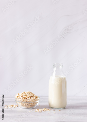Vegetable oat milk in a glass bottle and oat flakes on a light background. Healthy drinks, vegetarianism. Side view. Vertical photo