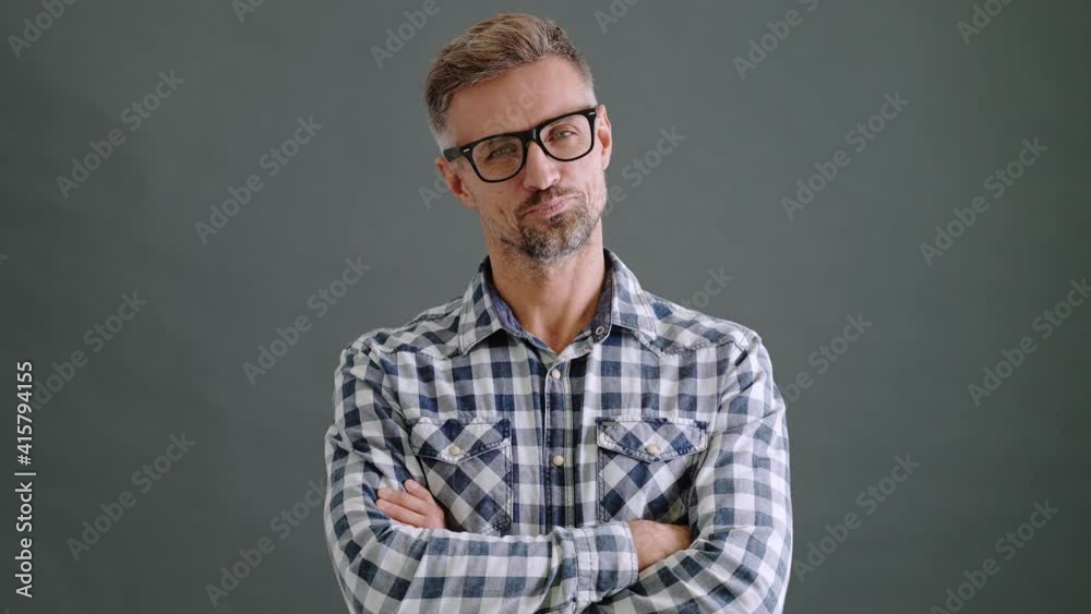 A handsome adult man wearing eyeglasses is looking to the camera standing in the confident pose isolated over a grey background in the studio A handsome adult man wearing eyeglasses is looking to the camera standing in the confident pose isolated over a grey background in the studio