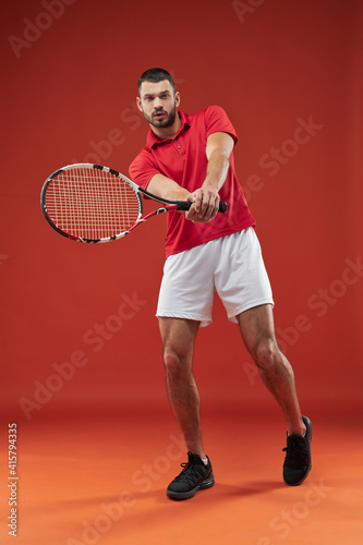 Handsome male tennis player with special tool in hands posing at the camera on red background photo