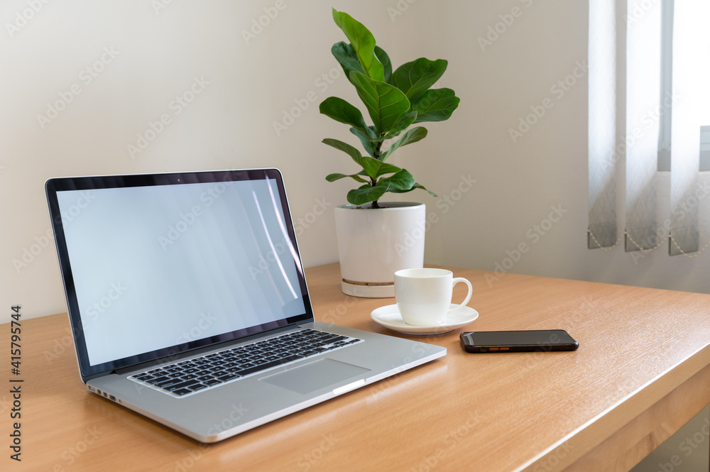 White screen Laptop computer with monstera plant, coffee cup and smart phone on wooden table White screen Laptop computer with monstera plant, coffee cup and smart phone on wooden table