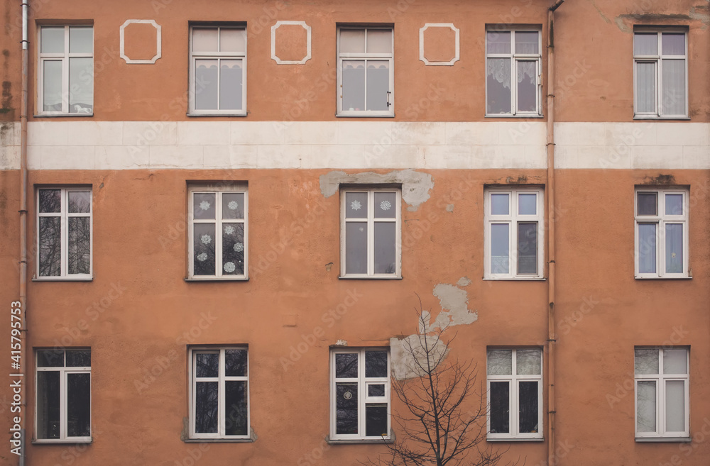 A part of yellow brown building facade with windows and a tree in front of it. Street view cityscape of Klaipeda city in Litrhuania. Retro hipster faded style of processing. Grey and gloomy mood