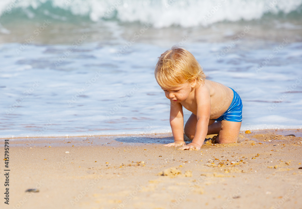 Little blond toddler boy crawl on the sand beach near sea waves Little blond toddler boy crawl on the sand beach near sea waves