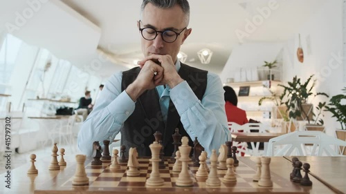 A close-up cropped view of a handsome man is playing chess sitting inside
