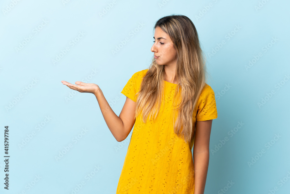 Young hispanic woman over isolated blue background holding copyspace with doubts Young hispanic woman over isolated blue background holding copyspace with doubts