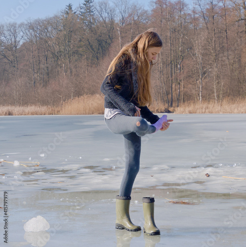 the girl looks at a wet sock on the lake ice 