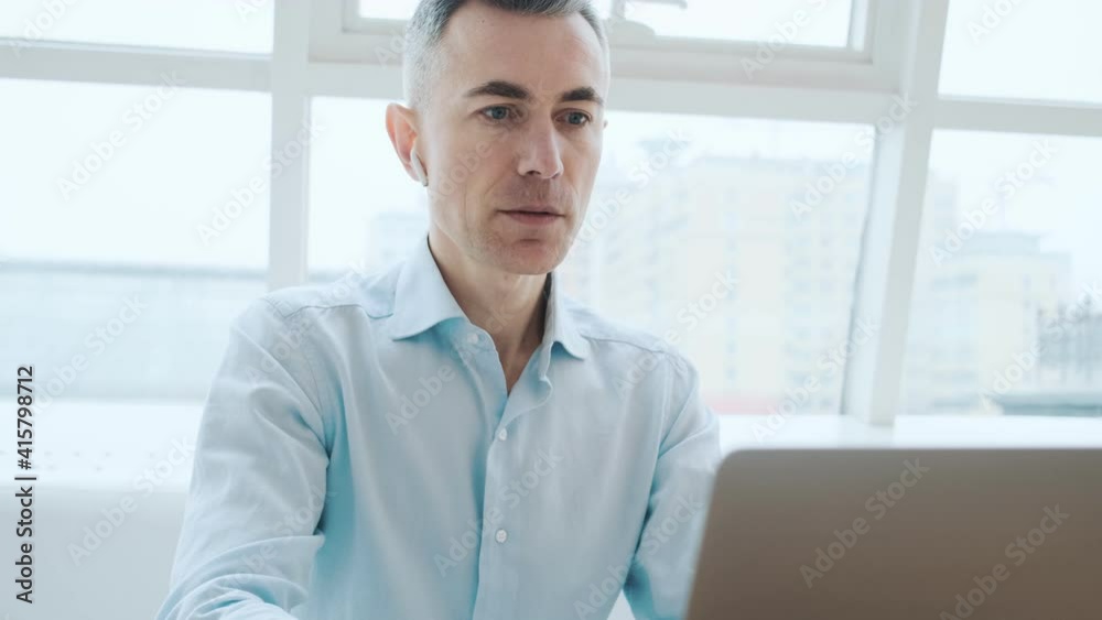 A confident adult man is doing winner gesture while using his laptop computer sitting inside the public space A confident adult man is doing winner gesture while using his laptop computer sitting inside the public space