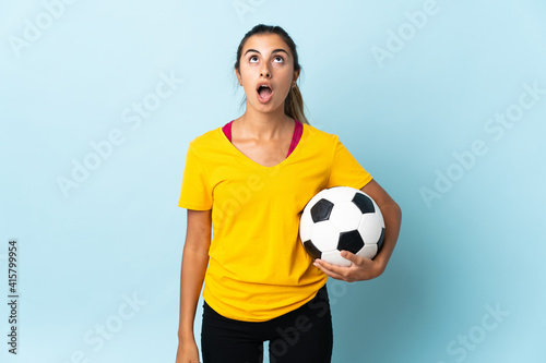 Young hispanic football player woman over isolated on blue background looking up and with surprised expression © luismolinero
