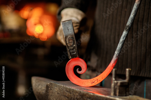 Slika na platnu Close-up of the hands of a blacksmith twisting a spiral with a hammer, putting a red-hot iron blank on an anvil
