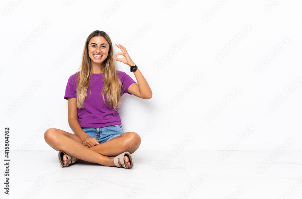 Young hispanic woman sitting on the floor showing ok sign with fingers