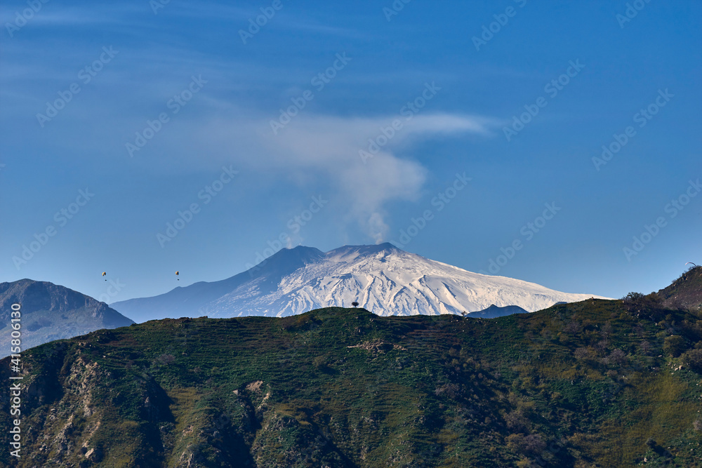 Obraz premium paragliding over the Etna volcano on a beautiful sunny day while the mountain smokes