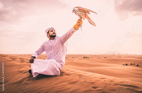 Arabic man with traditional emirates clothes walking in the desert with his falcon bird