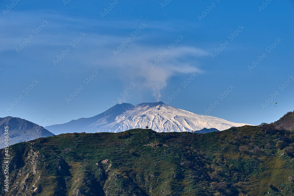 paragliding over the Etna volcano on a beautiful sunny day while the mountain smokes